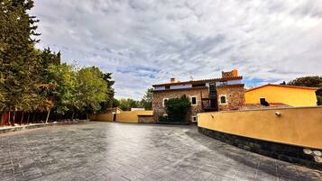 A courtyard with a stone wall, a building with a tiled roof, and trees.