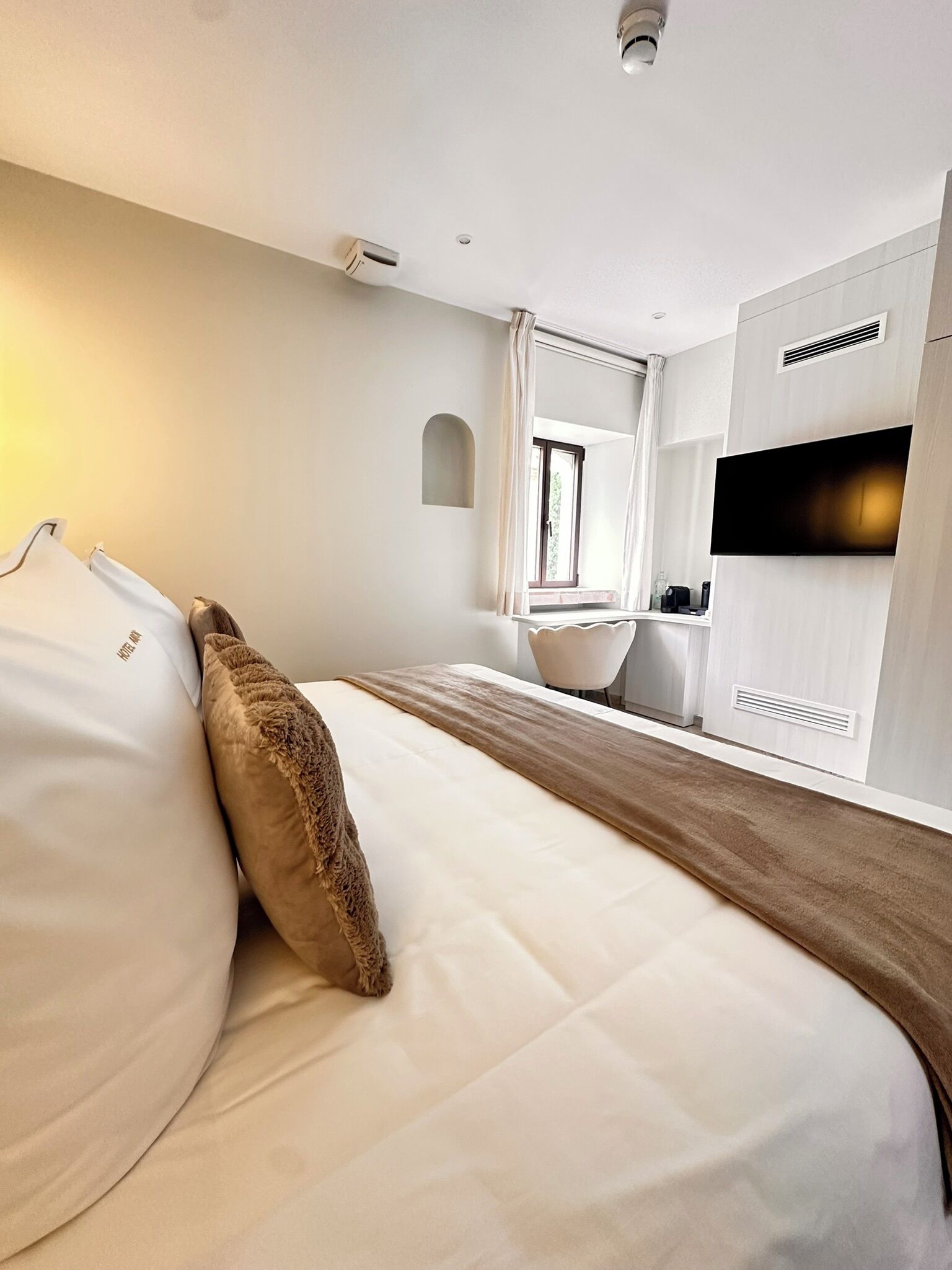 Habitación de hotel moderna con una cama grande, una ventana pequeña, un televisor de pantalla plana y un espacio con kitchenette.