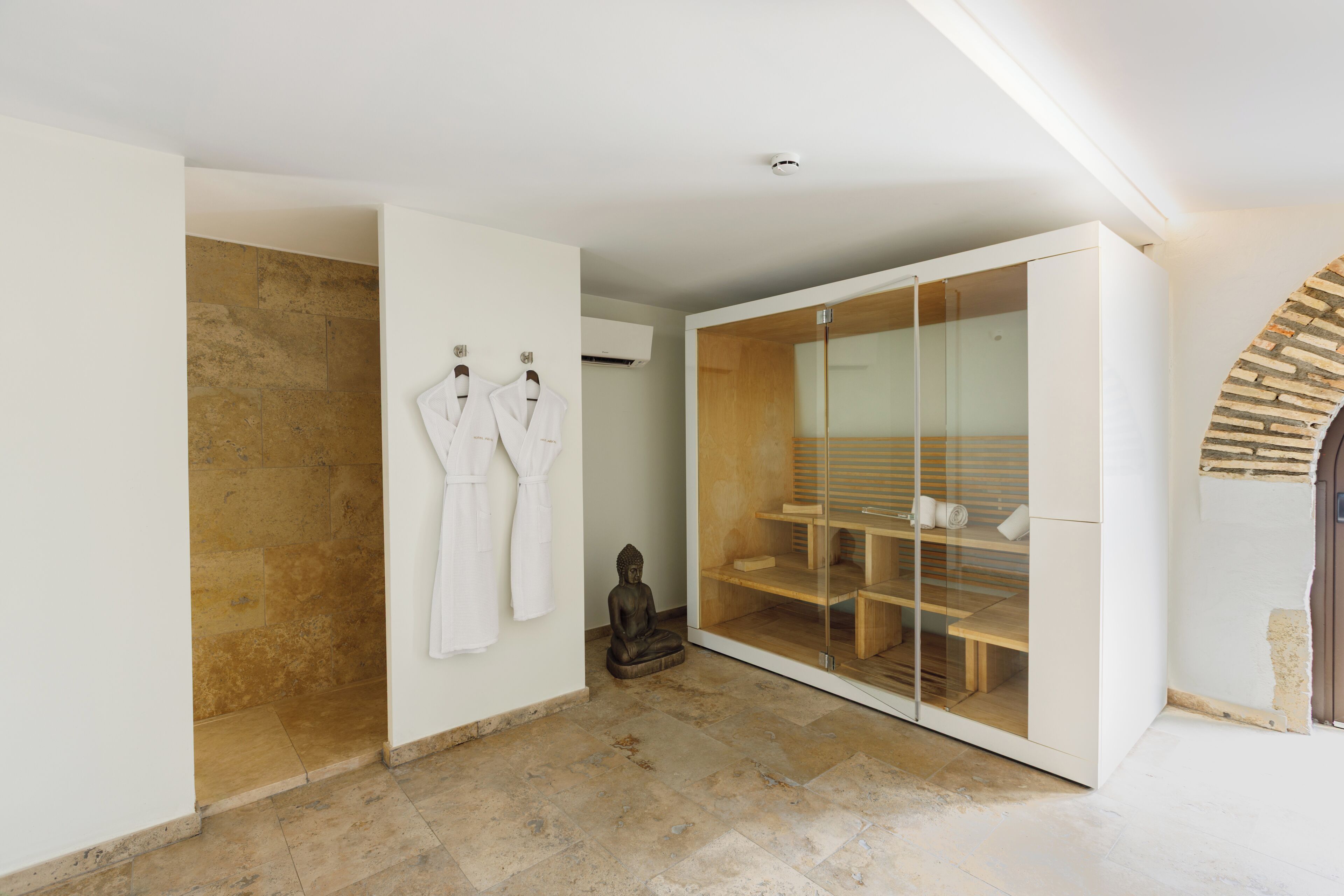 Une salle de bain moderne avec une douche en pierre, un dressing ouvert délimité par des parois de verre et une statue.