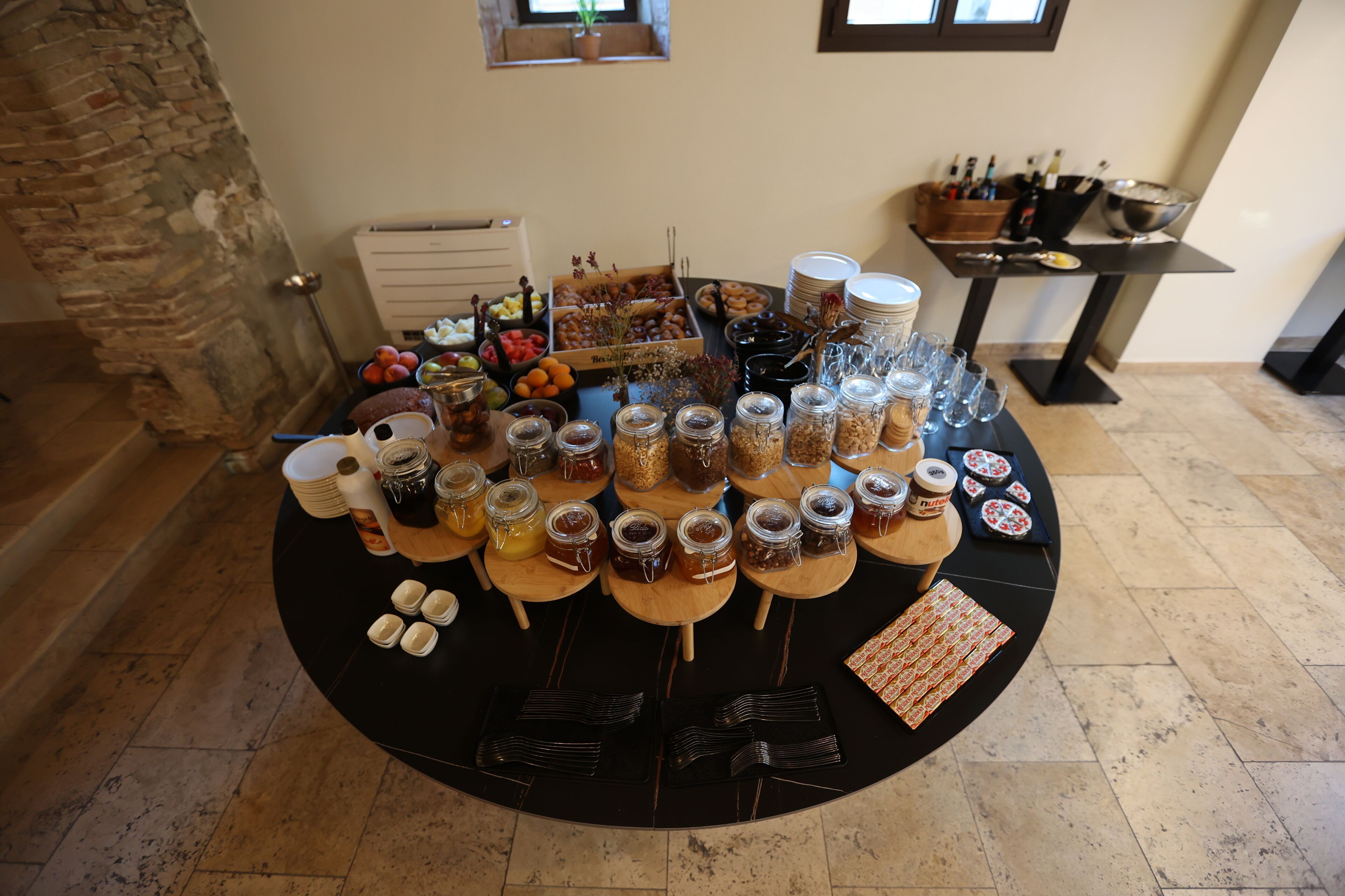 A buffet table with various food items, utensils, and glassware.