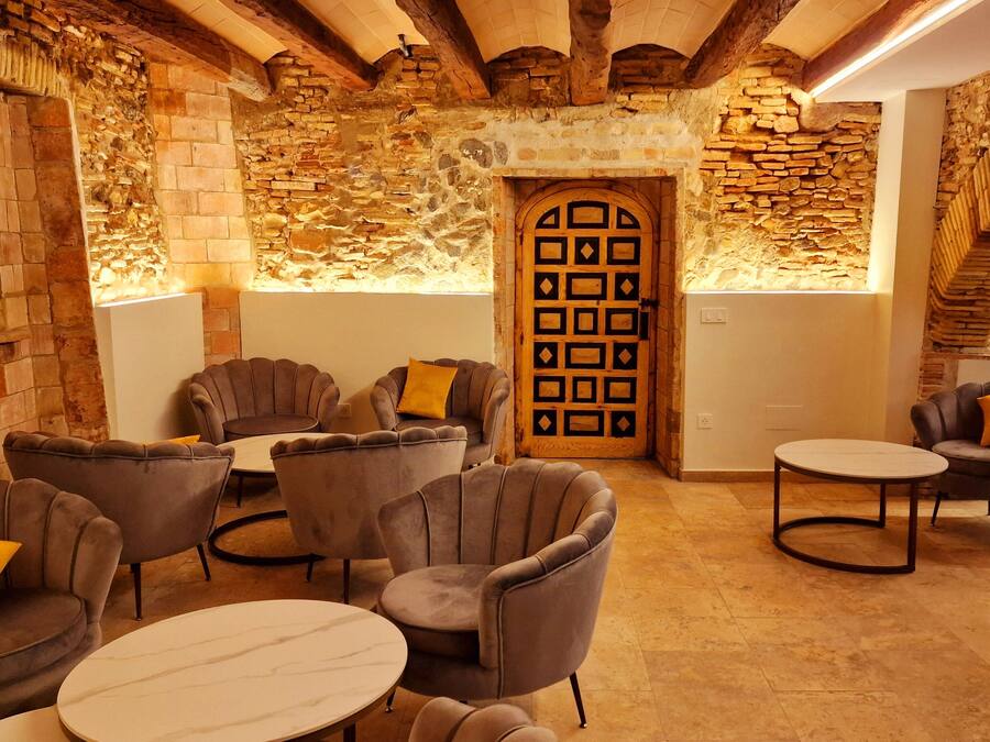 Un interior acogedor con paredes de piedra, una puerta de madera con diseños geométricos y muebles modernos, incluyendo sillones y mesas redondas.