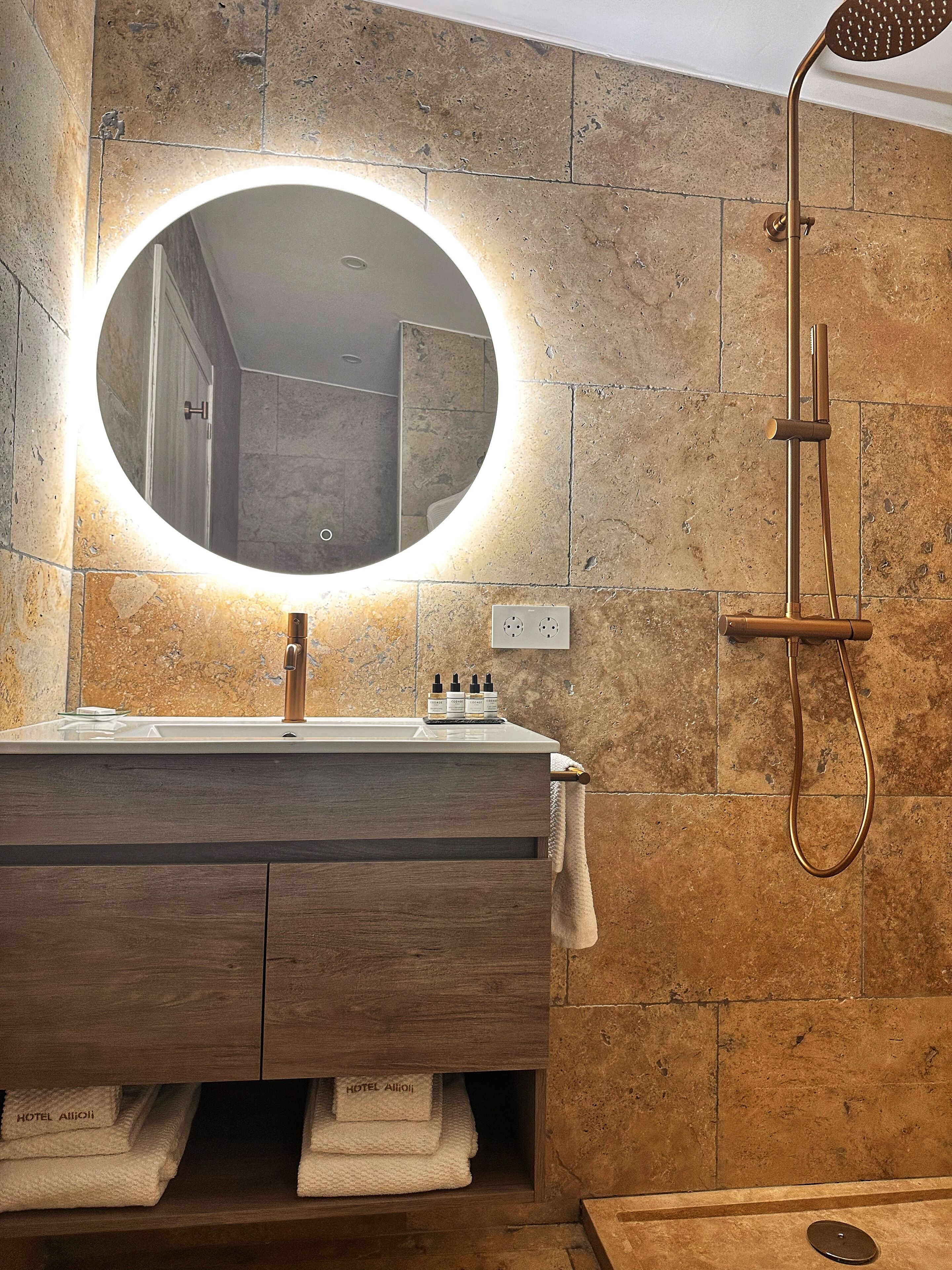 A bathroom with a round mirror, a wooden vanity, a towel rack, and a shower with a handheld showerhead.