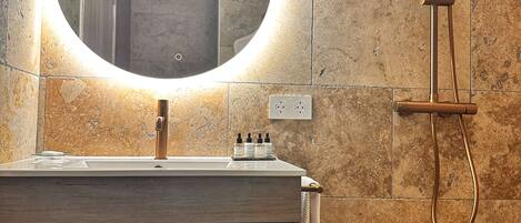 A bathroom with a round mirror, a wooden vanity, a towel rack, and a shower with a handheld showerhead.