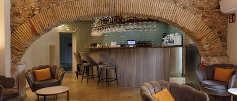 Zona de bar con arco de piedra, taburetes y mostrador con botellas y vasos.