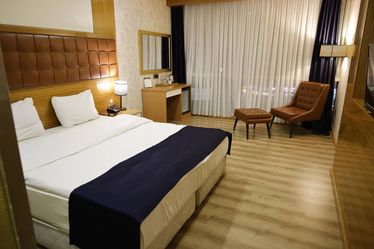 Camera d'albergo con un letto grande, una scrivania, una sedia e vista sulla città dalla finestra.