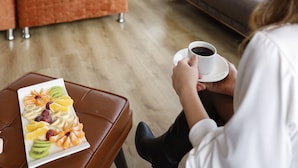 Una habitación de hotel moderna con cama, sofá, mesa de comedor con fruta y una taza de café.