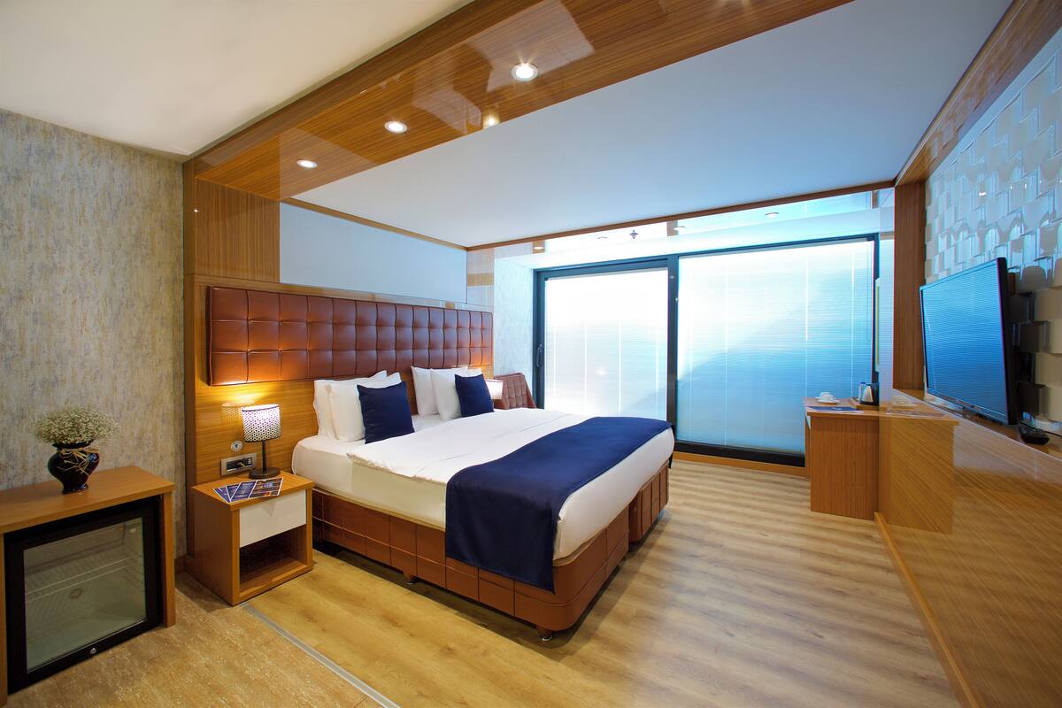 Una habitación de hotel moderna con una cama grande, televisión, escritorio y un amplio ventanal.