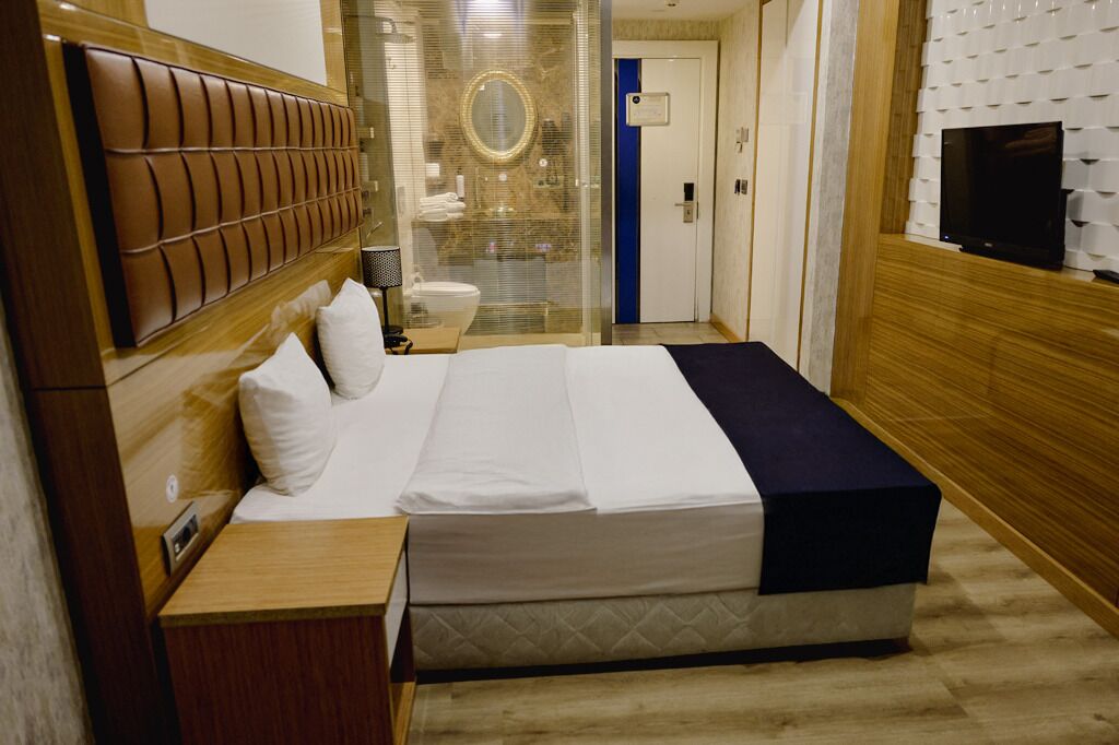 Una habitación de hotel con cama, mesita de noche y televisor fijado a la pared.