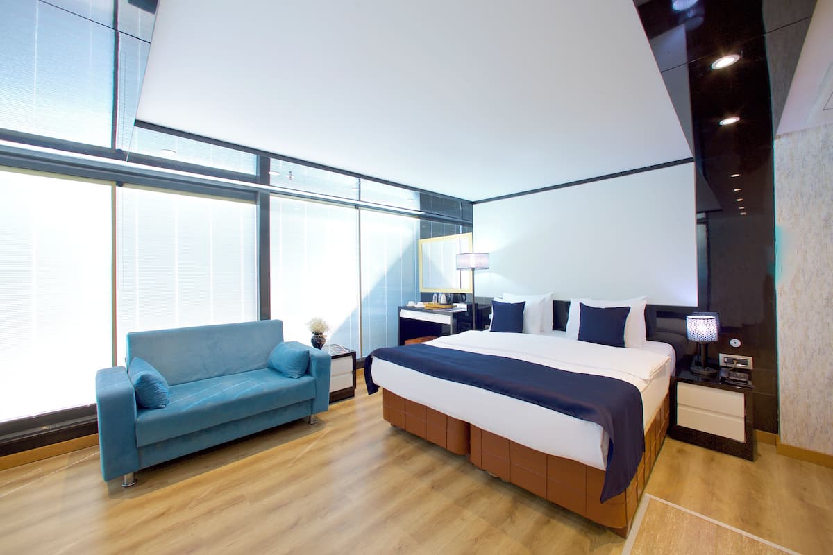 Una camera d'hotel moderna con un letto grande, un divano, una scrivania e una finestra con persiane.