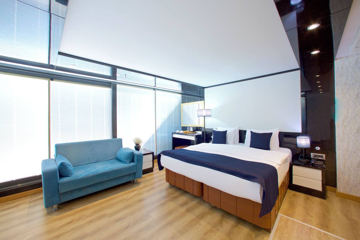 Una habitación de hotel moderna con una cama grande, un sofá, un escritorio y una ventana con persianas.