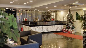 Zona de recepción de hotel con mostrador de mármol, un árbol de Navidad y alfombra roja.