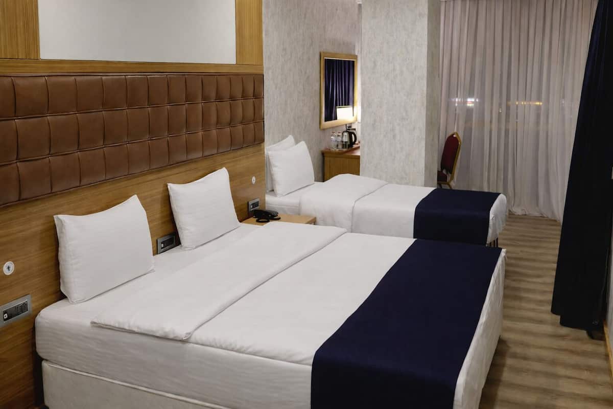 Una camera d'albergo con due letti, una testiera in legno, un comodino con una lampada e una finestra con tende.