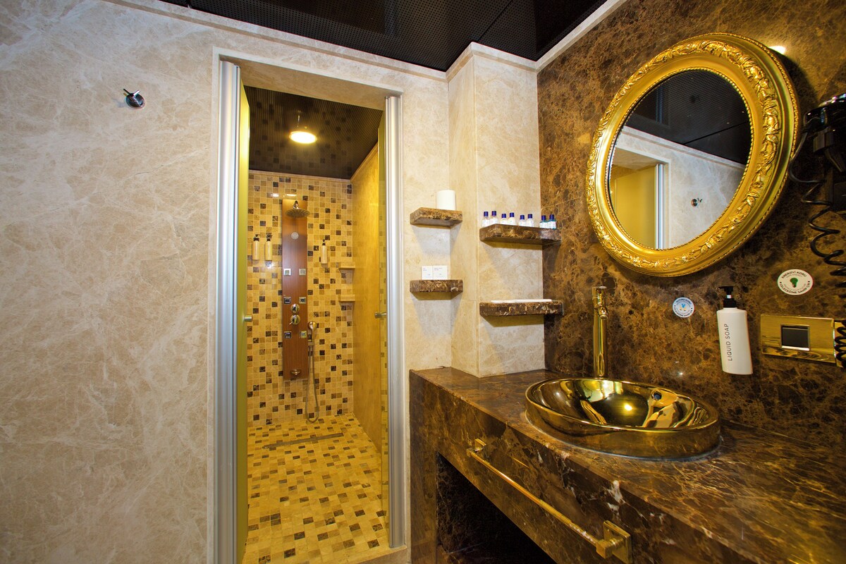 A bathroom with a shower, a sink with a gold basin, and a mirror with a gold frame.