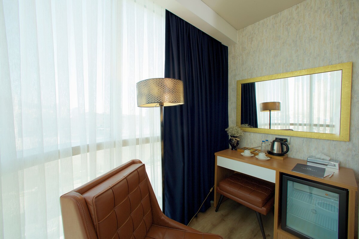 A hotel room with a desk, a chair, a television, and a large window with curtains.