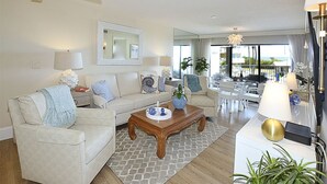 Een ruime woonkamer met een bank, salontafel en een eethoek. Een groot raam biedt uitzicht op de omgeving.