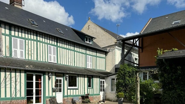 Een traditioneel vakwerkhuis met een groen-witte gevel, een kleine tuin en een helderblauwe lucht.