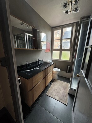 Une salle de bain moderne avec un lavabo noir, des meubles en bois, un miroir et une fenêtre.