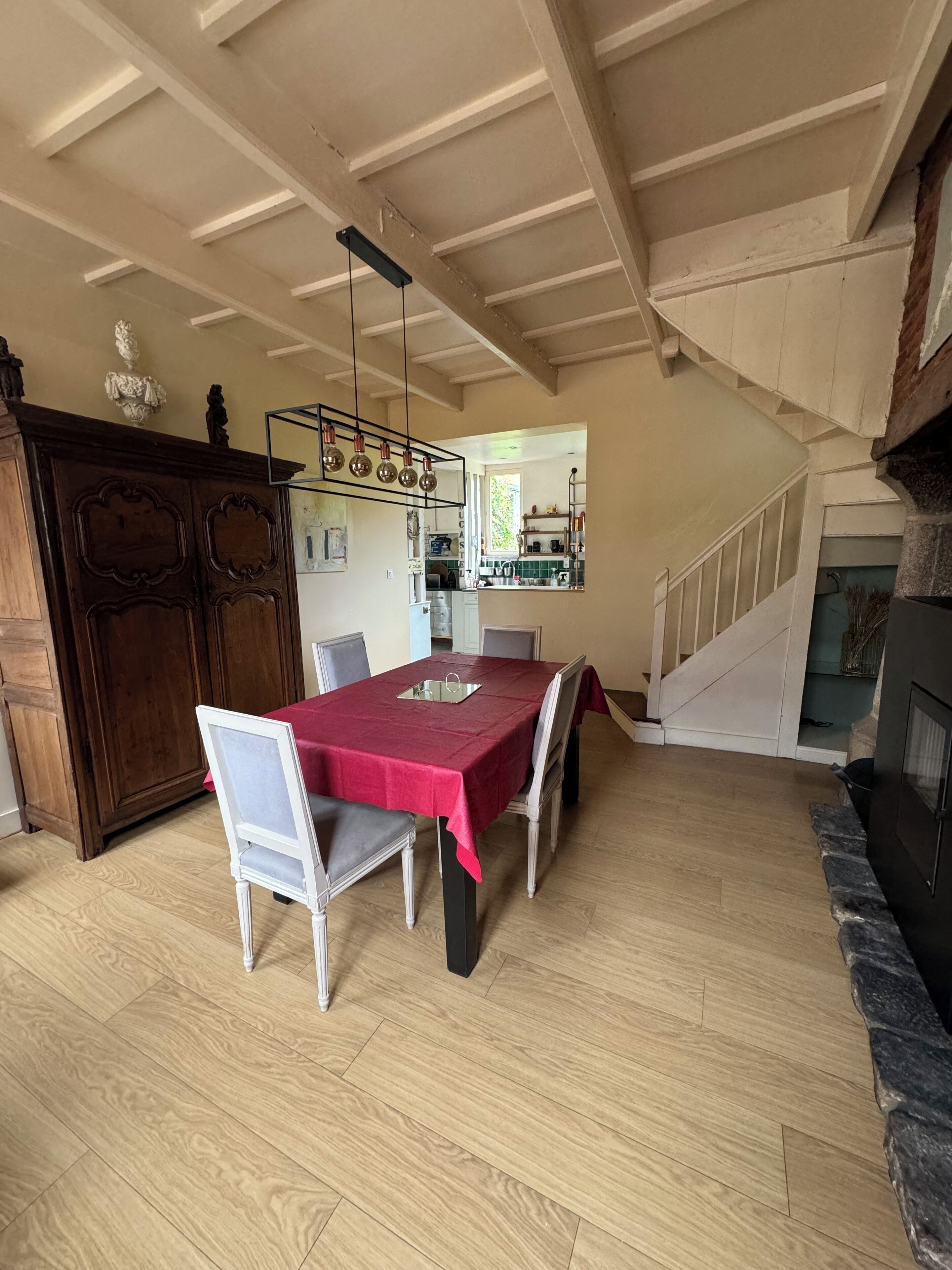 Un coin repas avec une table et des chaises en bois, une nappe rouge et un luminaire suspendu.