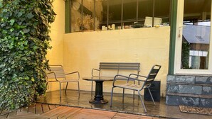 Een buitenpatio met een ronde tafel en vier stoelen, een bankje en een muur begroeid met klimop.