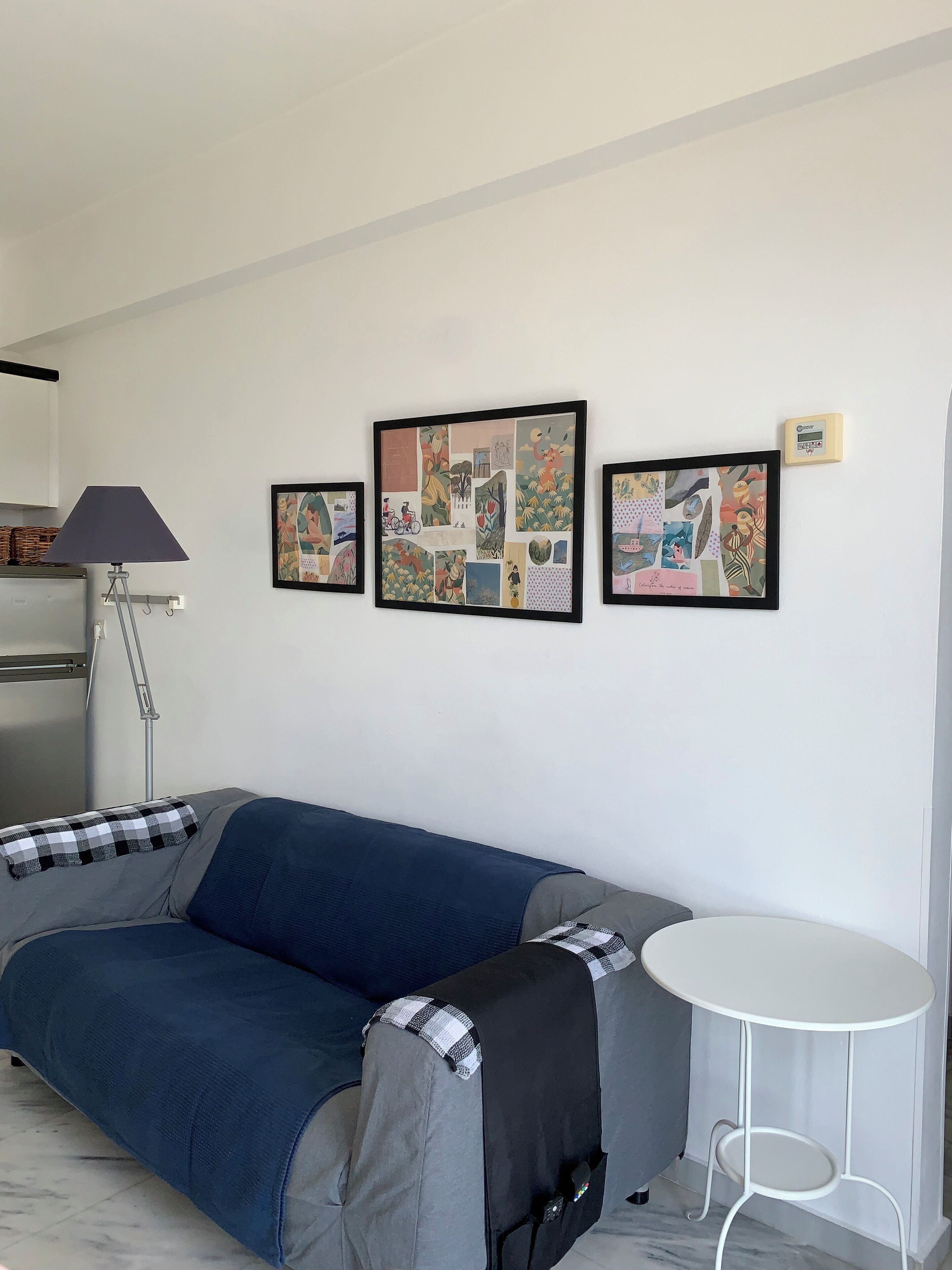 Ein modernes Wohnzimmer mit einem blauen Sofa, einem kleinen runden Tisch und drei gerahmten Kunstwerken an der Wand.