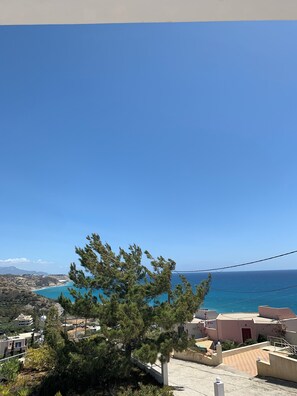 A coastal view with a clear sky, a pine tree in the foreground, and buildings with a beach in the background. - Villa Aliki (Ierapetra)