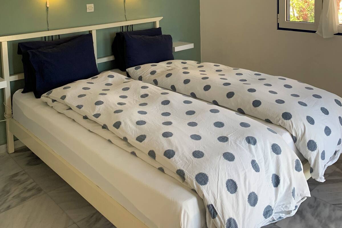 Ein Schlafzimmer mit zwei Betten, einem Deckenventilator, gerahmten Bildern und einem Fenster mit Vorhängen.