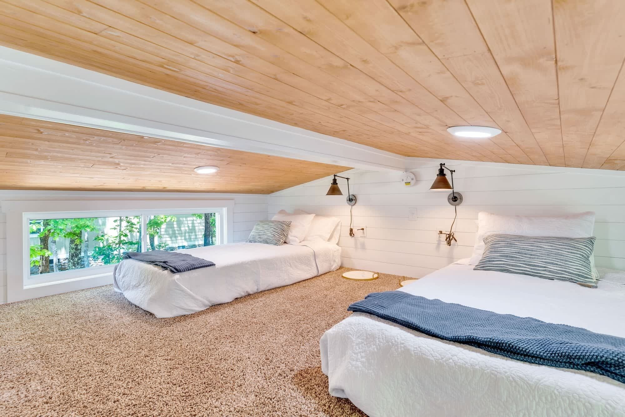 Ein gemütliches Schlafzimmer im Dachgeschoss mit zwei Betten, Holzbalken an der Decke und einem großen Fenster mit Blick auf Grünflächen.