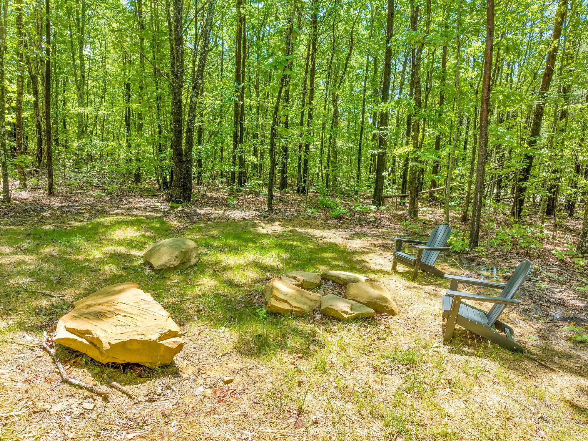 Um camping numa floresta, com uma rocha grande, duas cadeiras Adirondack e uma mesa de piquenique.