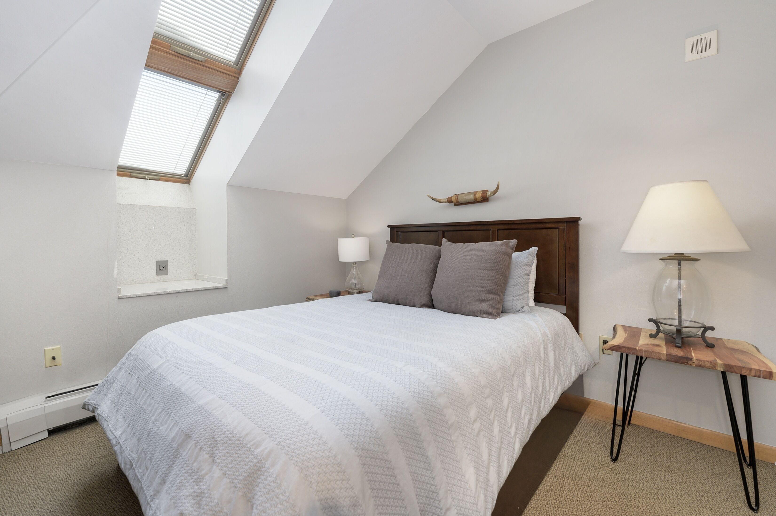 Une chambre avec un plafond en pente, un lit doté d’une tête de lit en bois, deux lampes de chevet et une petite table avec une lampe.