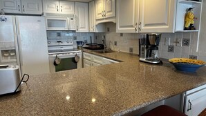 A kitchen with white cabinets, a granite countertop, a coffee maker, and a bowl on the counter. - Ocean Hideaway 610 2 Bedroom Condo by RedAwning (Ocean City)