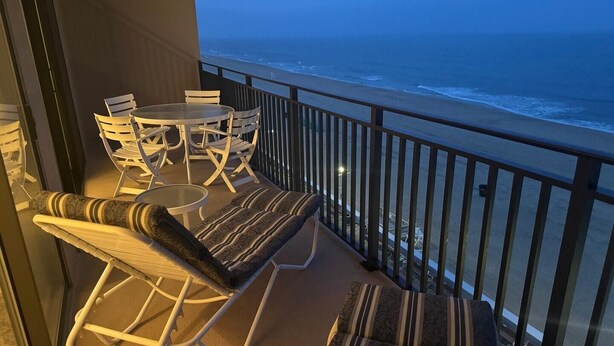 A balcony with a view of the ocean, furnished with a table, chairs, and a sofa. - Ocean Hideaway 610 2 Bedroom Condo by RedAwning (Ocean City)