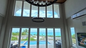 A room with large windows overlooking a pool and ocean view. - Sky Beach Club Rock House 4 Bedroom Home (Governor's Harbour)