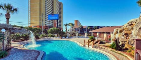 Un hotel con piscina, un cartel que dice "PORTSIDE" y un edificio alto al fondo.