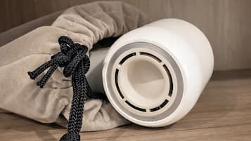 A white cylindrical object with a circular opening, placed on a wooden surface next to a beige fabric item with a black braided cord.
