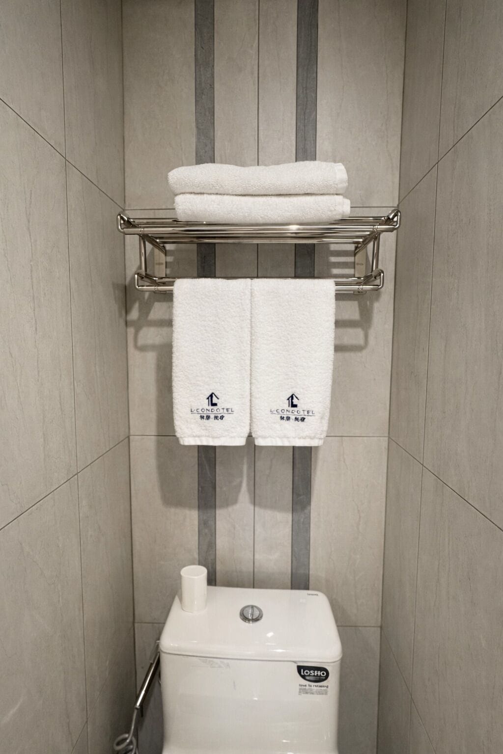 A bathroom with a toilet, a towel rack with two towels, and a wall with vertical stripes.
