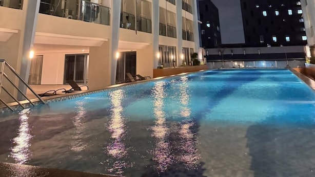 Un moderno edificio de gran altura con varios balcones, una piscina y un cielo despejado al anochecer.