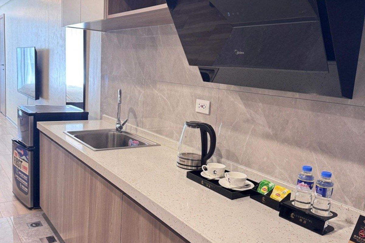 A modern kitchen with a stainless steel sink, a coffee maker, and a tray with cups and bottled water.