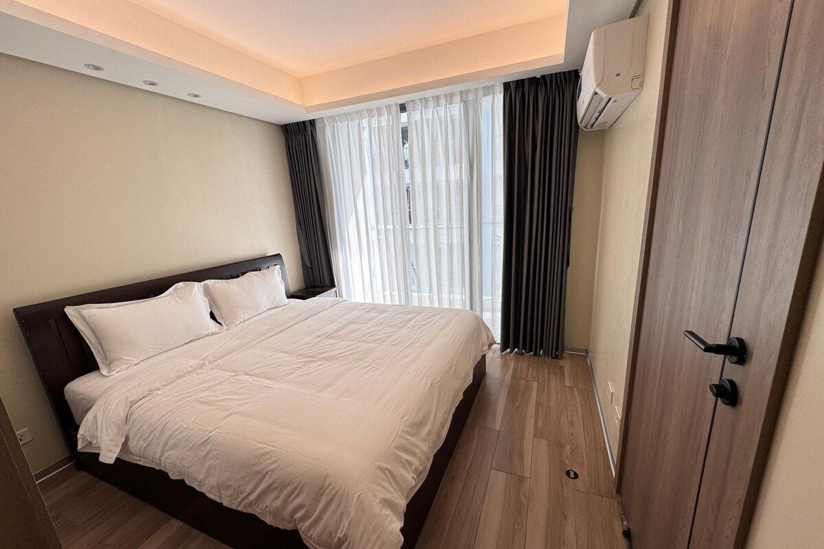 Ein Schlafzimmer mit Bett, Kleiderschrank, einem Fenster mit Vorhängen und einer Klimaanlage.