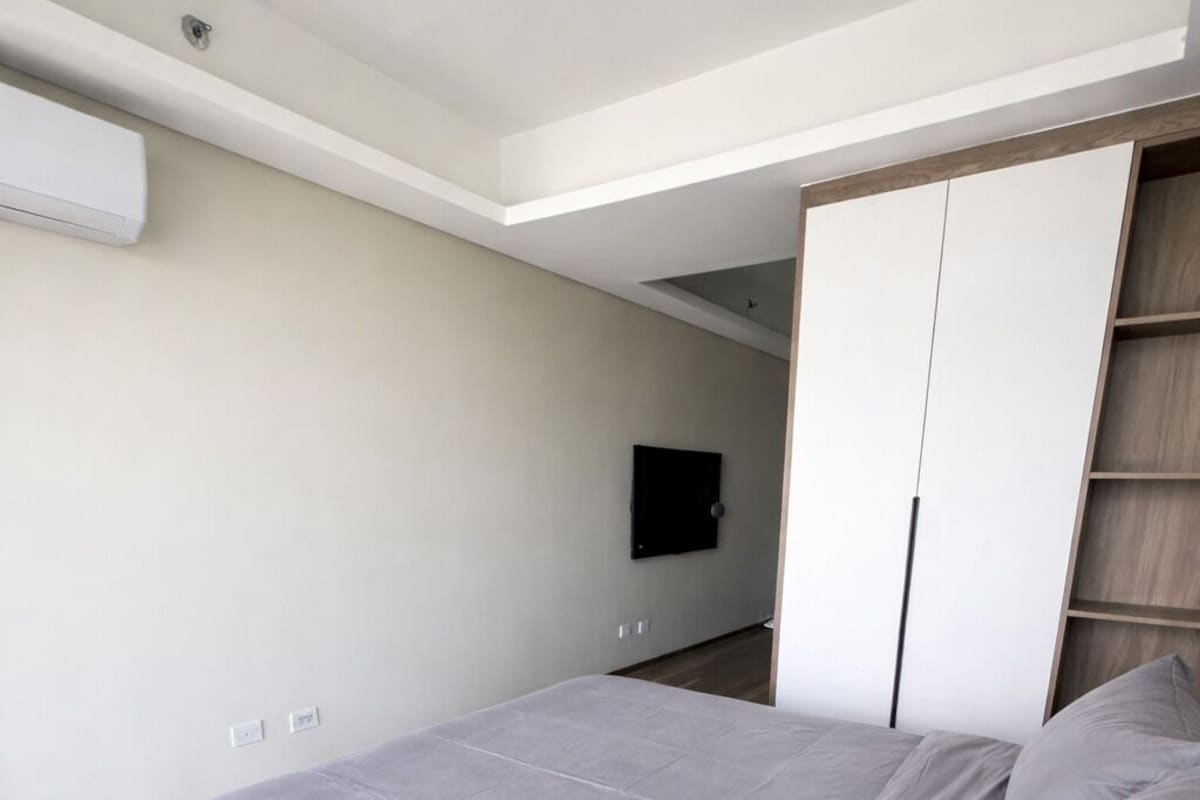 A bedroom with a bed, a wardrobe, a television, and an air conditioning unit.