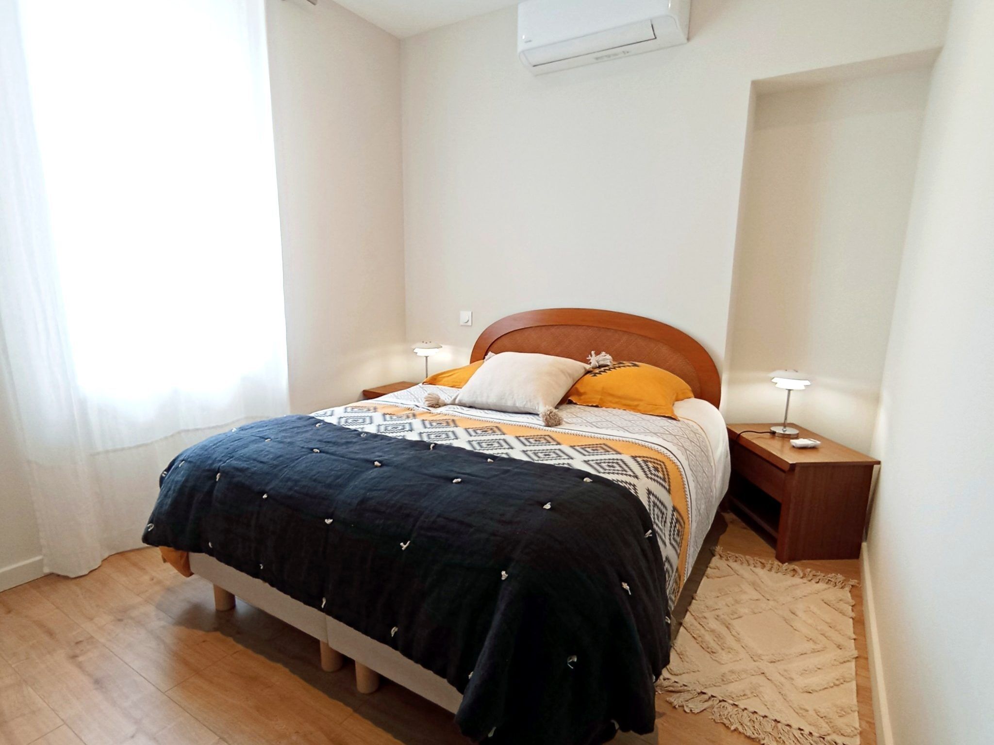 Ein Schlafzimmer mit einem Bett, zwei Nachttischen, einer Decke mit Muster und einem Teppich.