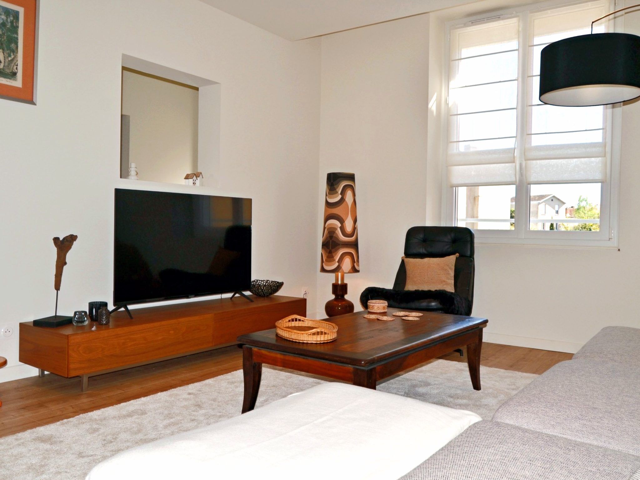 A living room with a TV, wooden furniture, a window, and a lamp.