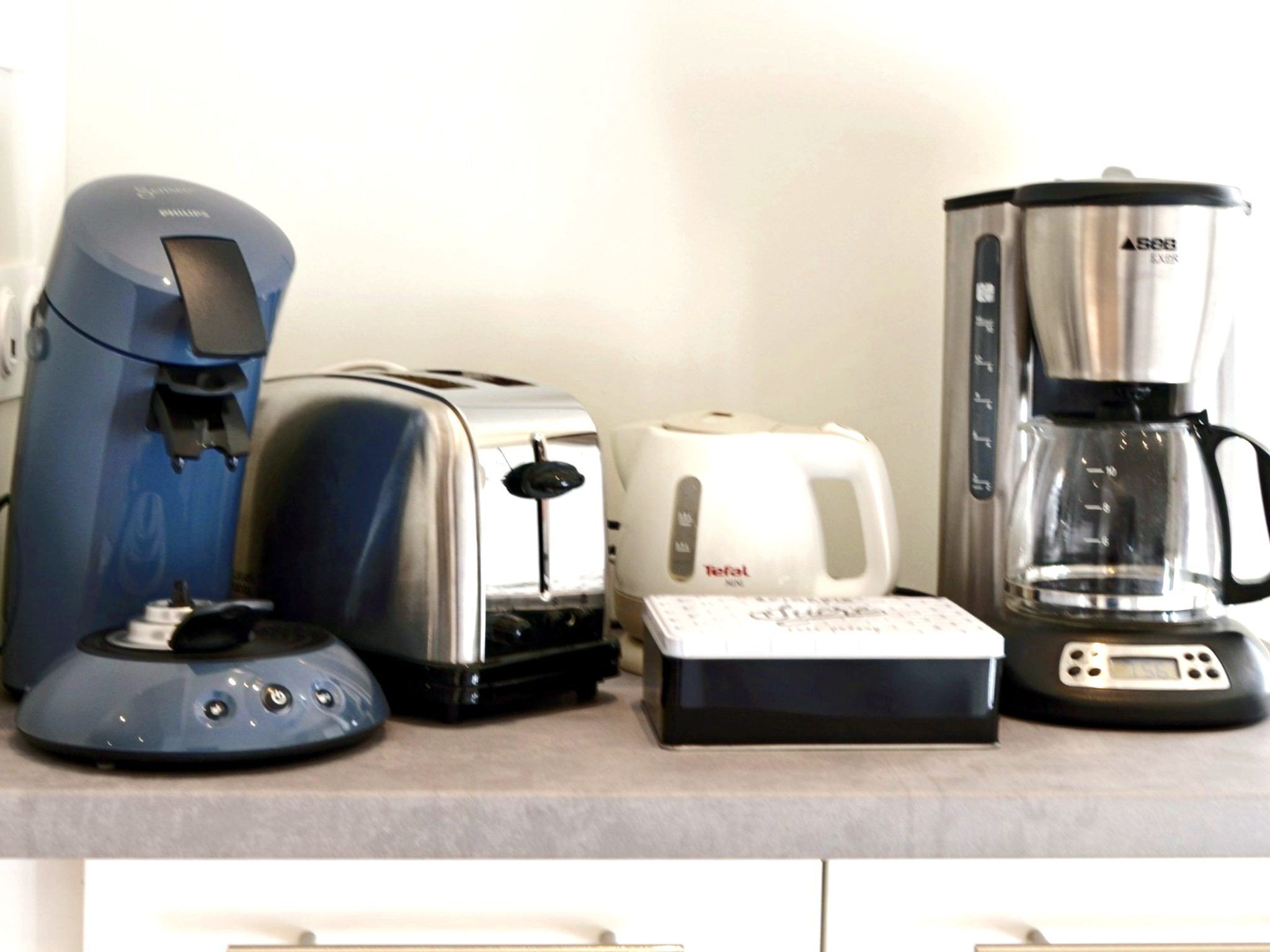 Eine Küchenarbeitsplatte mit einer blauen Kaffeemaschine, einem Toaster, einem weißen Wasserkocher und einer Kaffeekanne.