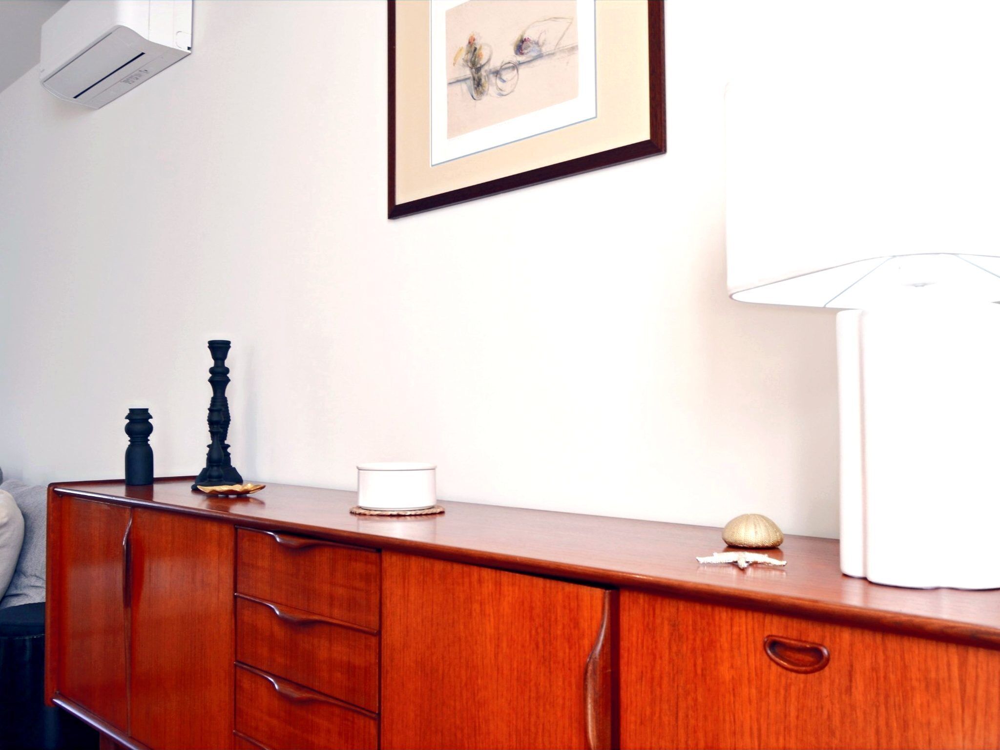 Una cassettiera in legno con cassetti, un quadro appeso al muro e una lampada sul mobile.