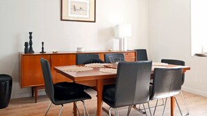 A dining area with a wooden table, black chairs, a white lamp, and a framed picture on the wall.