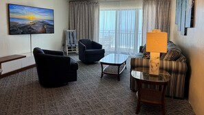 Ein Hotelzimmer mit großem Fenster, einer Couch, einem Sessel, einem kleinen Tisch und einem an der Wand befestigten Fernseher.