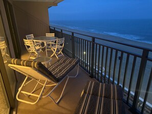 Een balkon met uitzicht op de oceaan, een tafel en stoelen, en een zithoek met kussens.