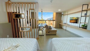A modern hotel room with a balcony, a dining area, and a TV on the wall.