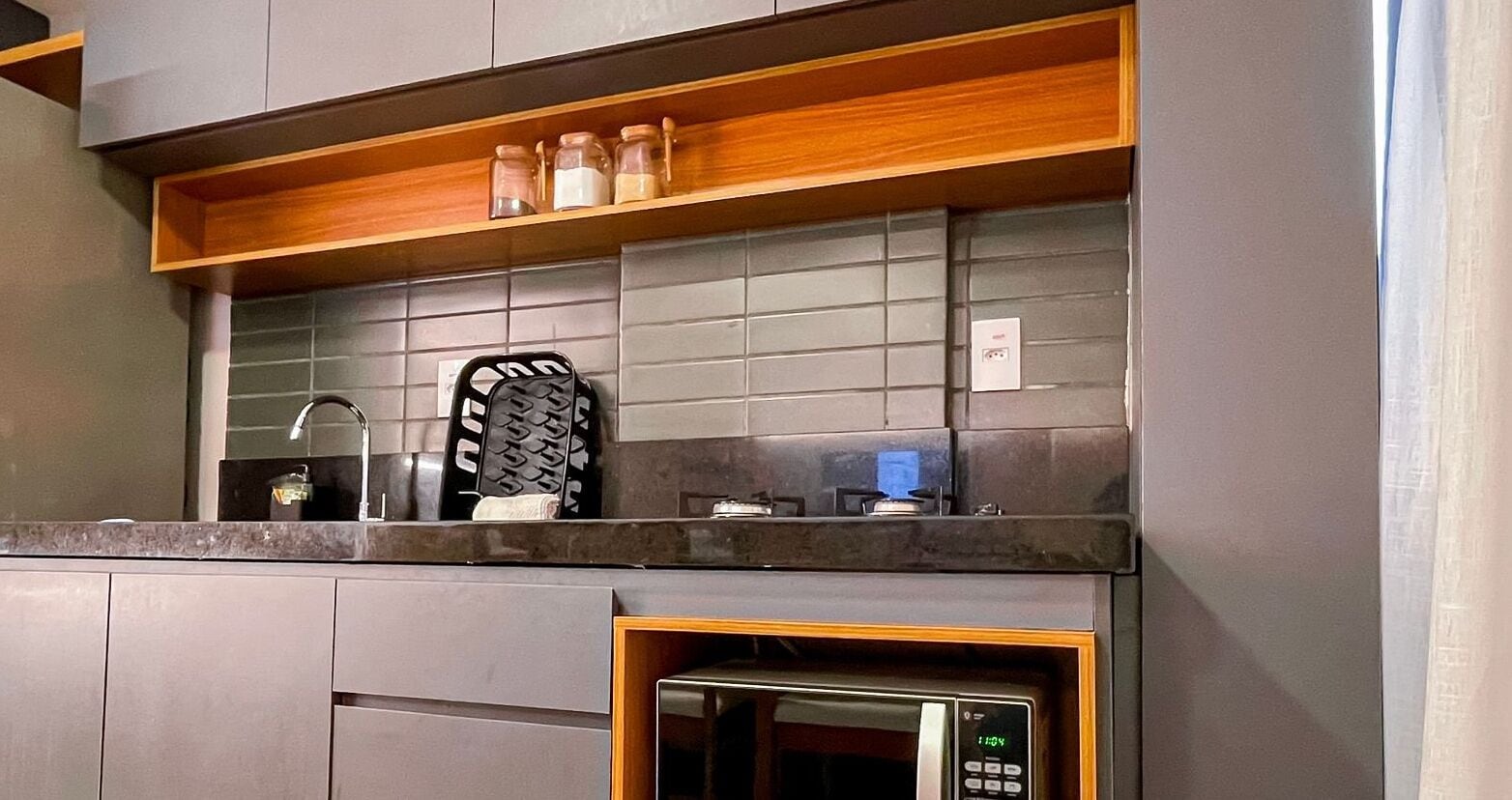 Una cocina moderna con gabinetes grises, un estante de madera y un microondas empotrado.