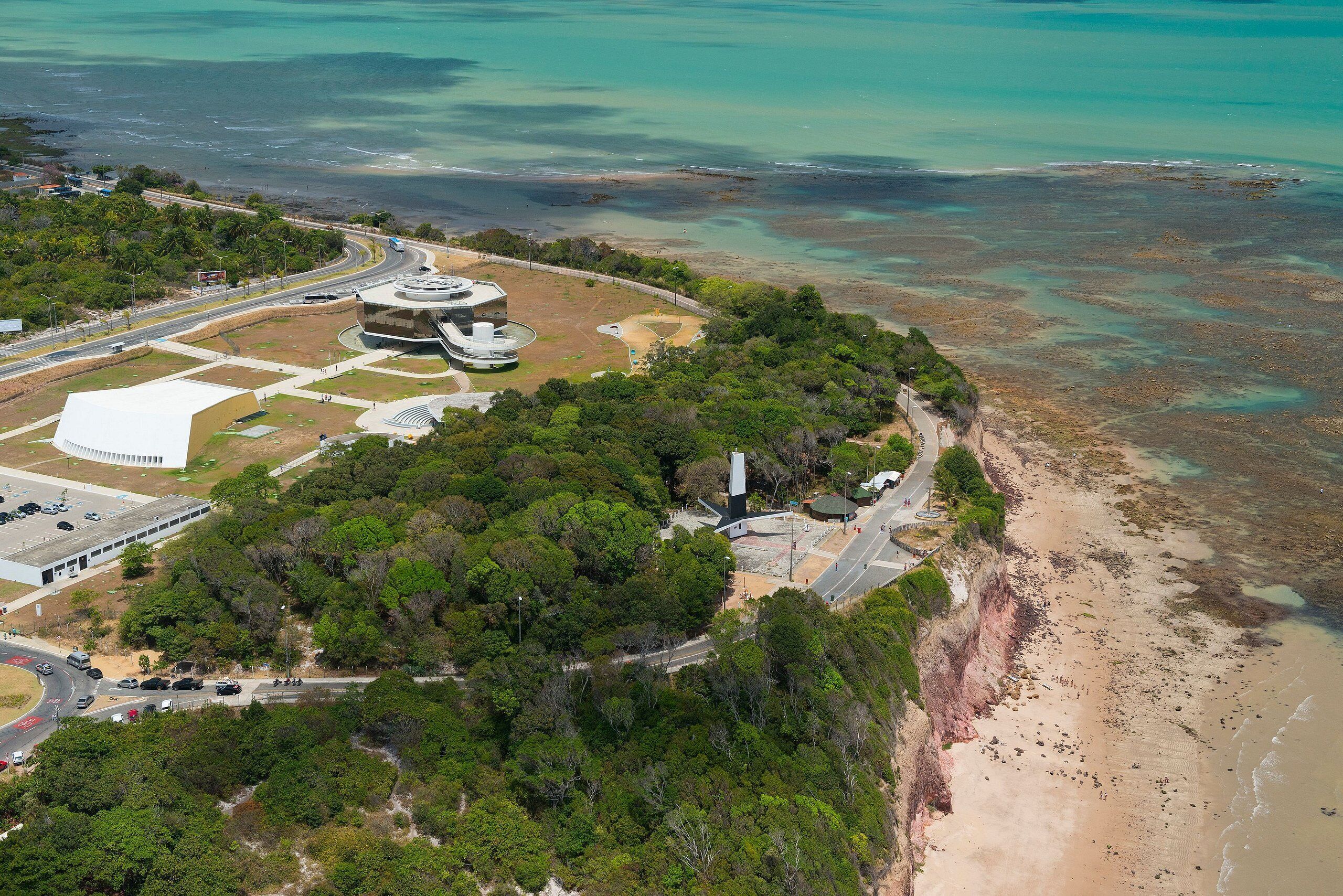 An aerial view of a coastal area with a large building complex, roads, and a beach.