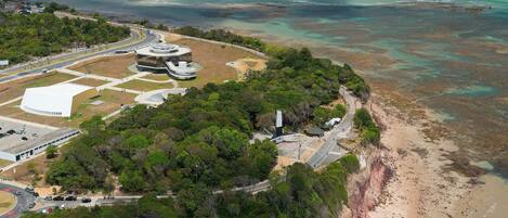 An aerial view of a coastal area with a large building complex, roads, and a beach.